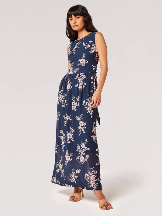 A woman posing in a sleeveless navy floral Apricot Blooms Maxi Dress with a belted waist and open-toe heels, perfect for her summer wardrobe.