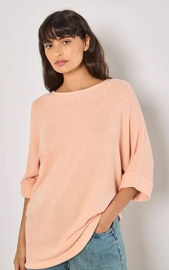 A person in a versatile Apricot Batwing Waffle Knit Top and blue jeans poses against a plain background, with one hand in their pocket.