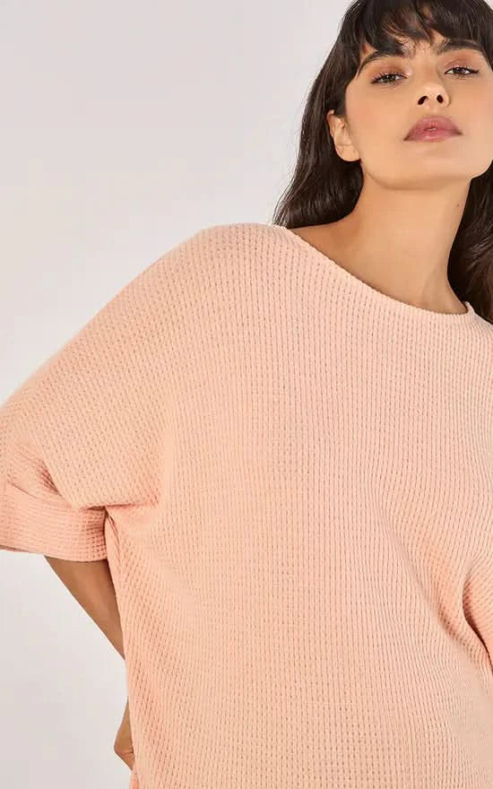 A person in a versatile Apricot Batwing Waffle Knit Top and blue jeans poses against a plain background, with one hand in their pocket.