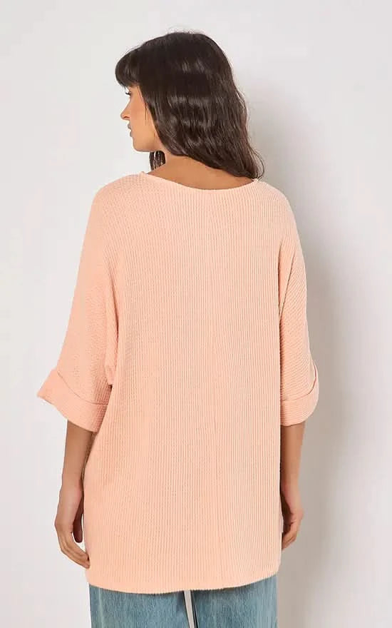 A person in a versatile Apricot Batwing Waffle Knit Top and blue jeans poses against a plain background, with one hand in their pocket.