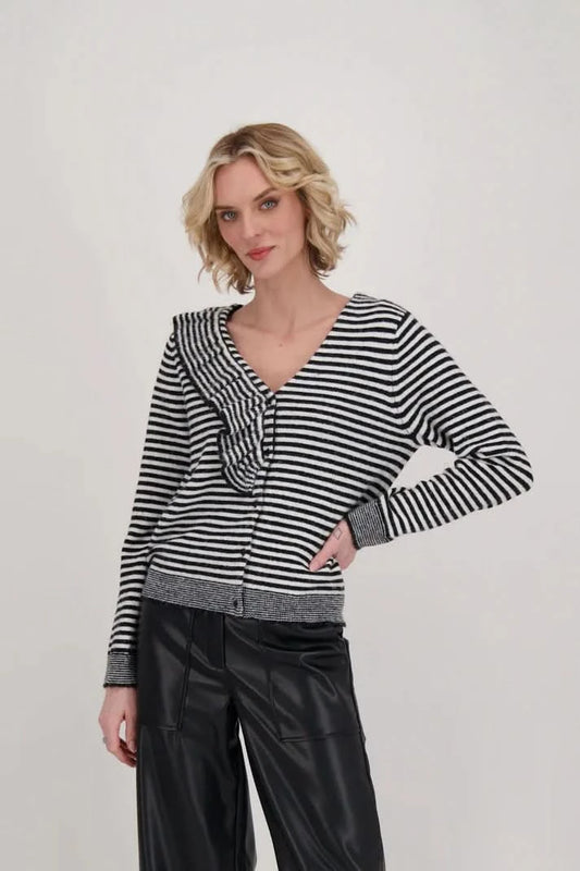 A woman dressed in a Gabby Isabella Ruffle Neck Stripe Sweater Top with black and white accents and black leather pants stands against a plain background.
