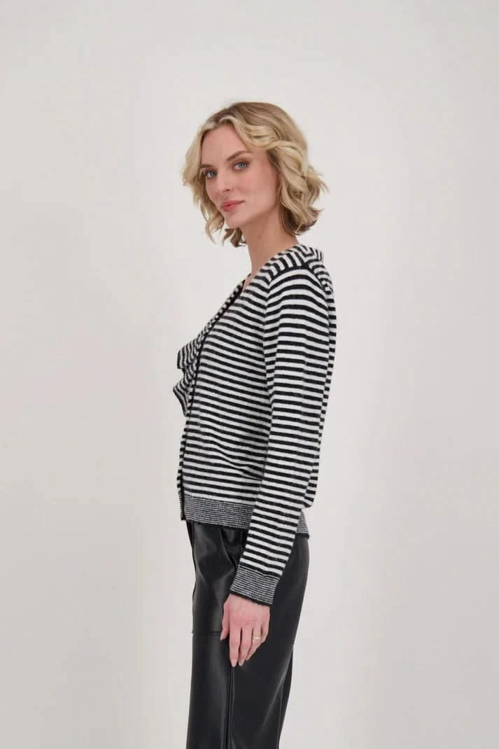 A woman dressed in a Gabby Isabella Ruffle Neck Stripe Sweater Top with black and white accents and black leather pants stands against a plain background.