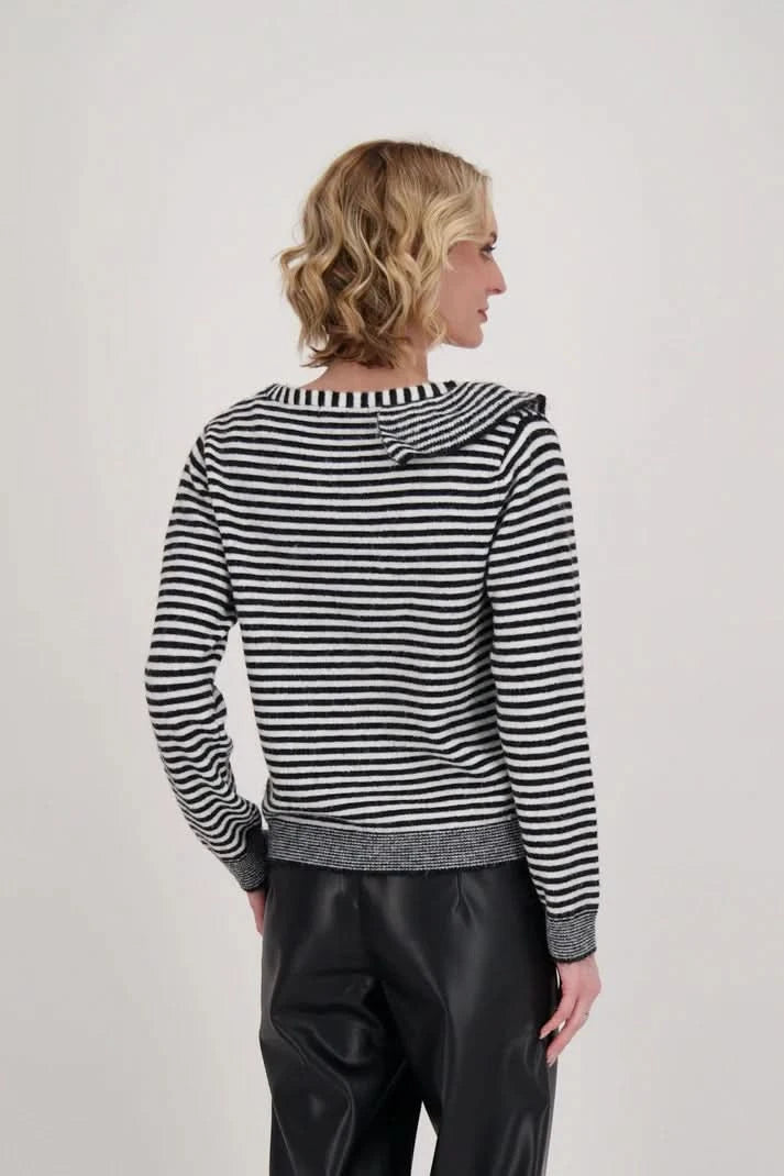 A woman dressed in a Gabby Isabella Ruffle Neck Stripe Sweater Top with black and white accents and black leather pants stands against a plain background.