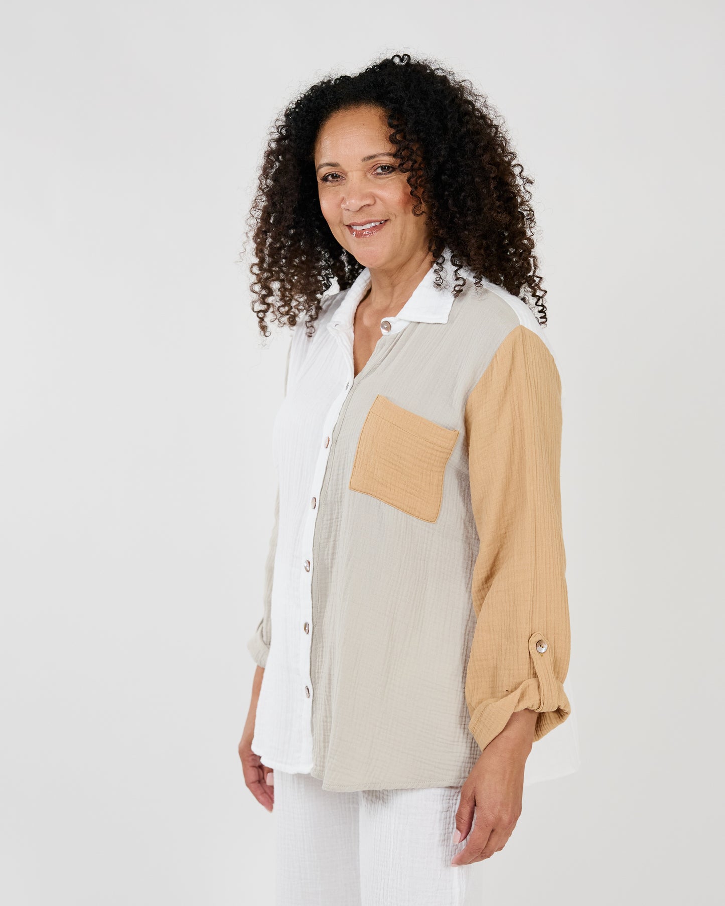 A woman with curly hair smiling, wearing a Shannon Passero Malani Button Up Shirt and white pants against a light background.