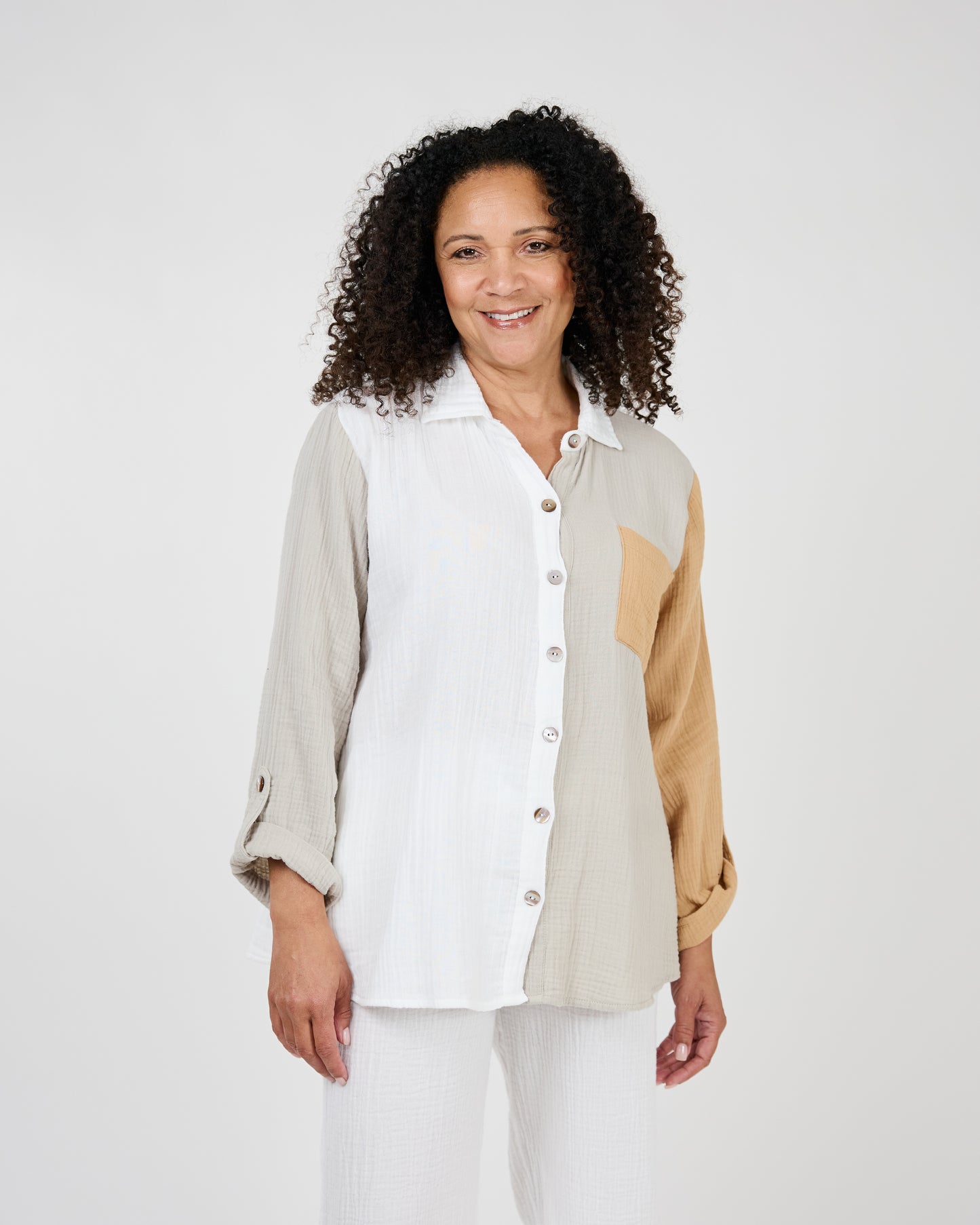 A woman with curly hair smiling, wearing a Shannon Passero Malani Button Up Shirt and white pants against a light background.