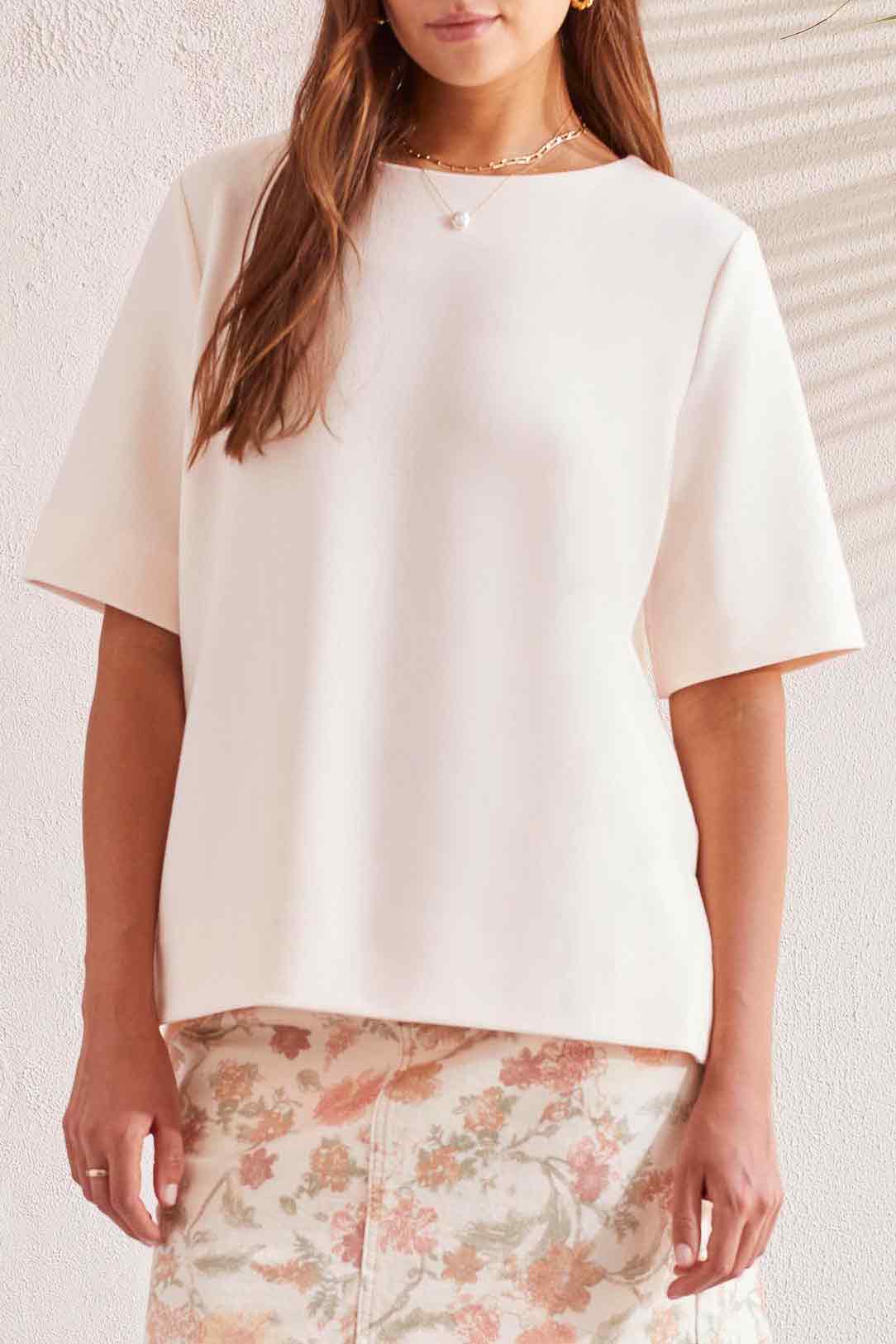 A close up of a woman wearing a white blouse with Tribal Elbow Sleeve Boat Neck With Side Slits and floral print pants.
