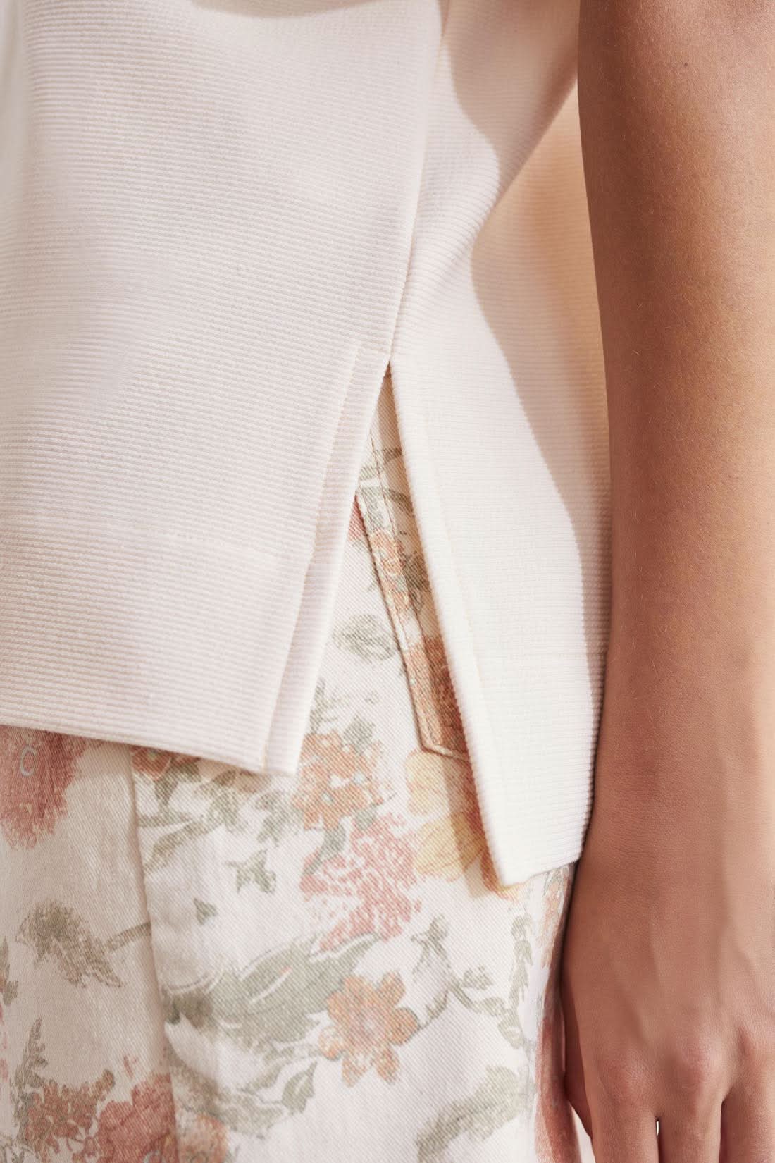 A close up of a woman wearing a white blouse with Tribal Elbow Sleeve Boat Neck With Side Slits and floral print pants.