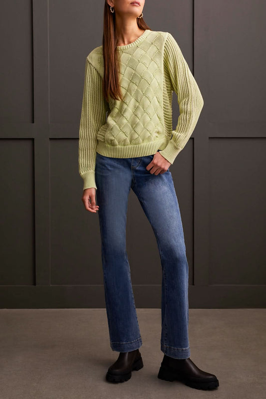 A person is wearing a light green Dolman Crew Neck Sweater with Special Wash from Tribal, along with blue jeans, standing against a dark wall. The luxurious comfort of the soft fabric is evident as the person's hand rests casually in one pocket.
