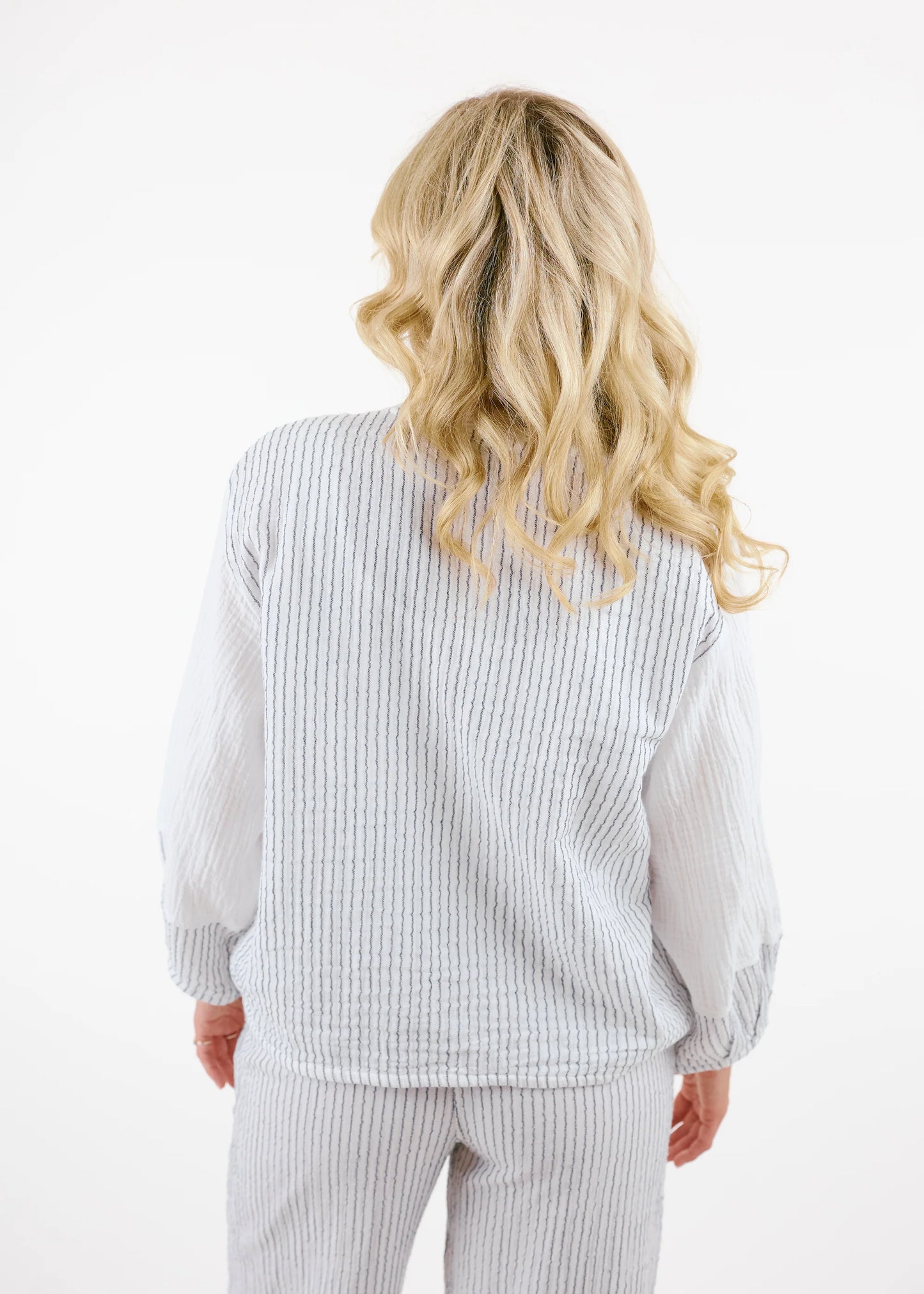 A woman with long blonde hair wears the Shannon Passero Kennedy Jlot—a white cotton gauze textured jacket with gray striped sleeves and matching pants—while standing against a plain white background.