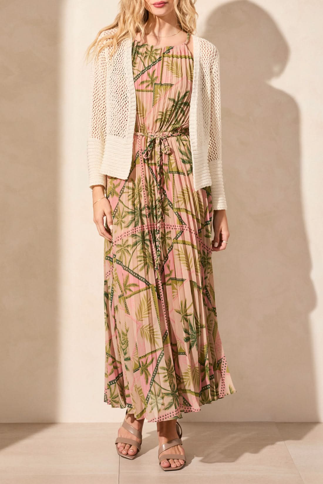 A person wears the "Tribal" crochet cardigan over a pink dress with a bamboo pattern. The BELL SLEEVE OPEN STITCH CARDIGAN features an open stitch design, offering luxurious comfort with textured sleeves and lightweight fabric.