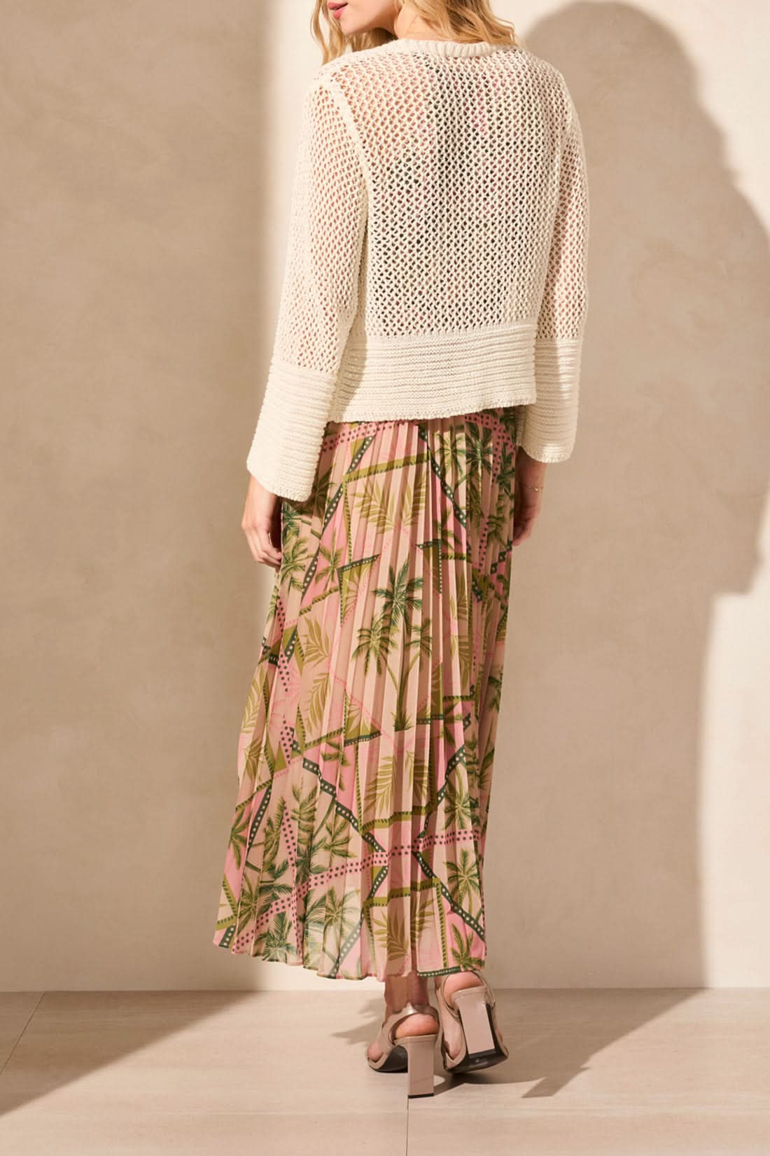 A person wears the "Tribal" crochet cardigan over a pink dress with a bamboo pattern. The BELL SLEEVE OPEN STITCH CARDIGAN features an open stitch design, offering luxurious comfort with textured sleeves and lightweight fabric.