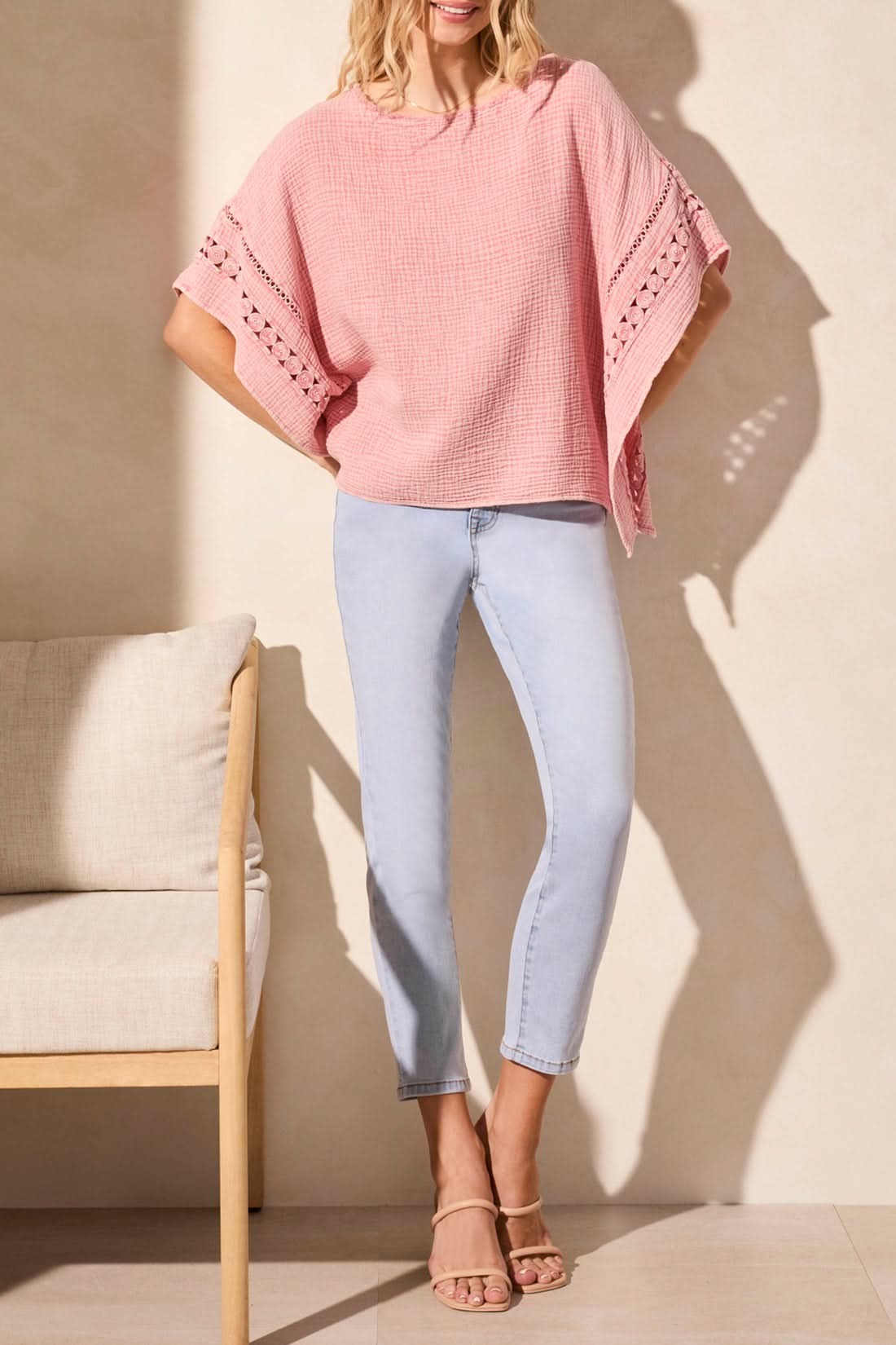 A stylish person confidently wears a Tribal KAFTAN BLOUSE in pink paired with light blue skinny jeans, standing near a beige chair on a light-colored floor.