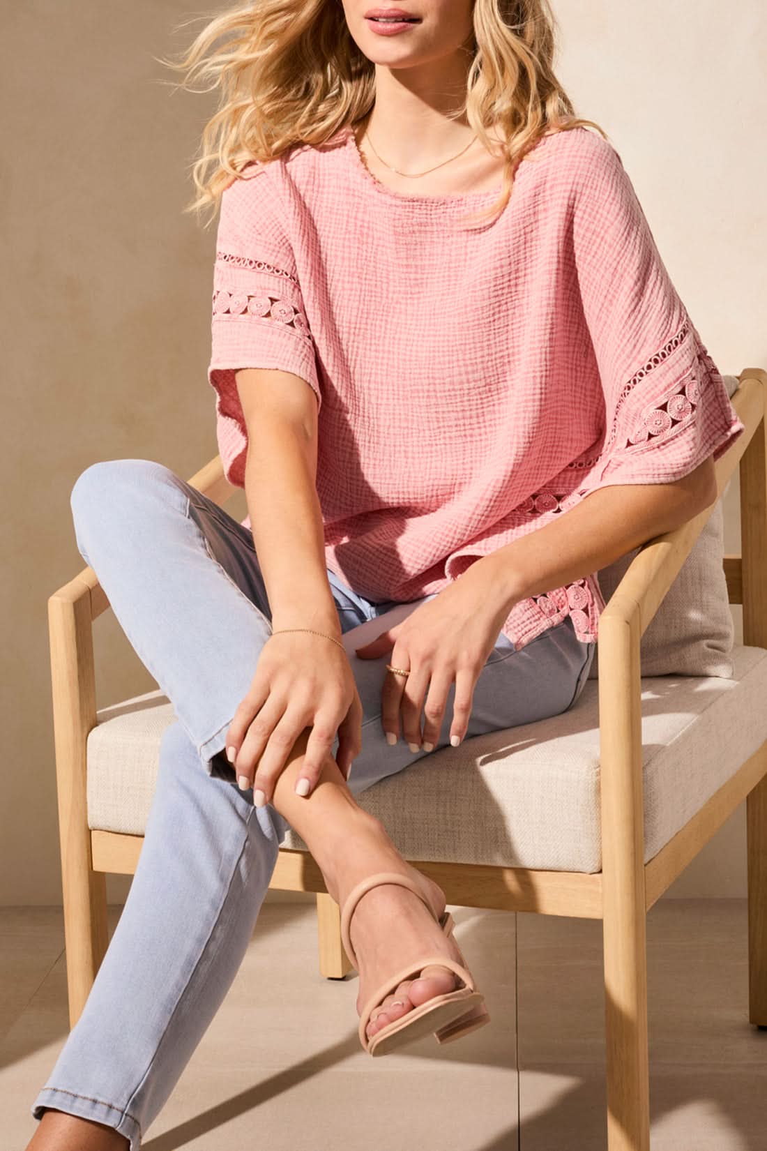A stylish person confidently wears a Tribal KAFTAN BLOUSE in pink paired with light blue skinny jeans, standing near a beige chair on a light-colored floor.