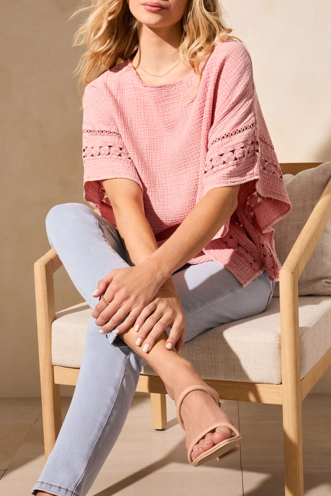A stylish person confidently wears a Tribal KAFTAN BLOUSE in pink paired with light blue skinny jeans, standing near a beige chair on a light-colored floor.