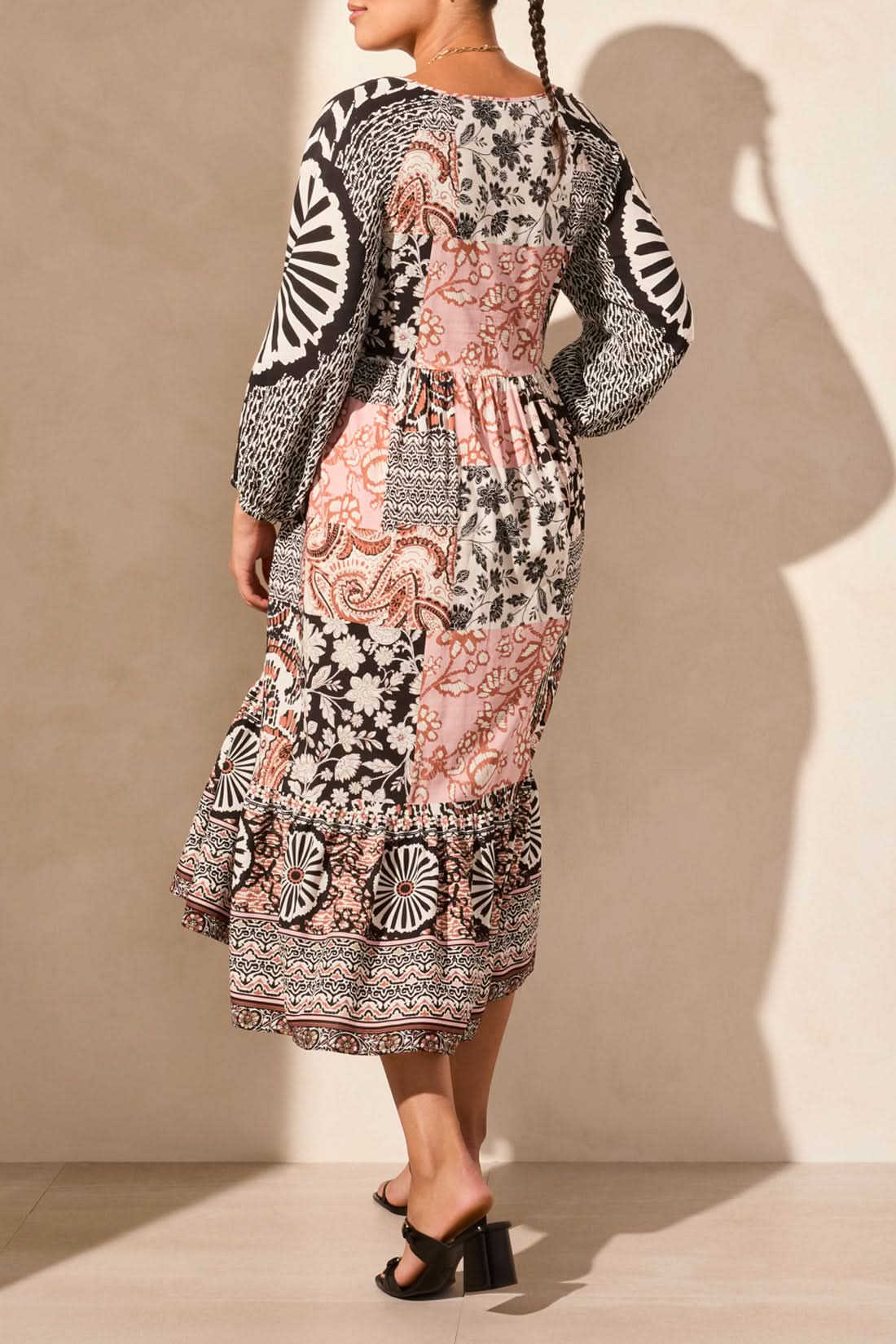 They are elegantly poised on a light floor, wearing the Tribal RAGLAN SLEEVE COMBO PRINT DRESS with 3/4 sleeves and a blend of black, white, and pink floral-geometric designs.
