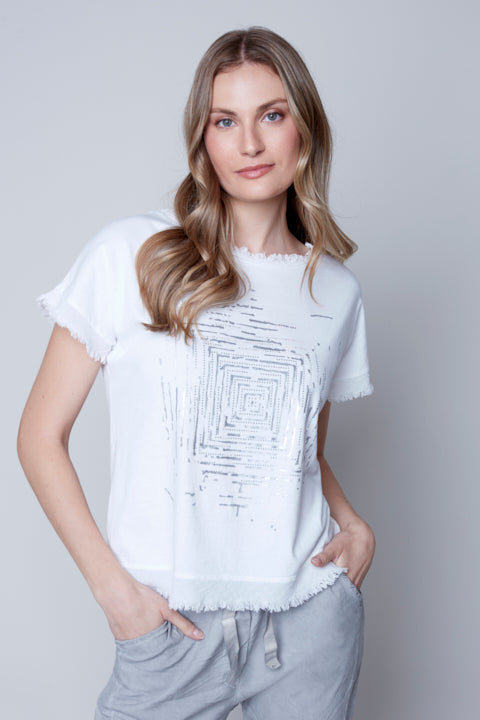 Woman posing in a versatile Carre Noir white Cowl Neck Frayed Tee with a graphic design and grey sweatpants against a neutral background.