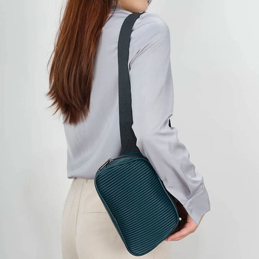 The Co-Lab Neoma sling bag features a small, rounded shape, teal vegan leather with a ribbed texture, and a wide black shoulder strap.