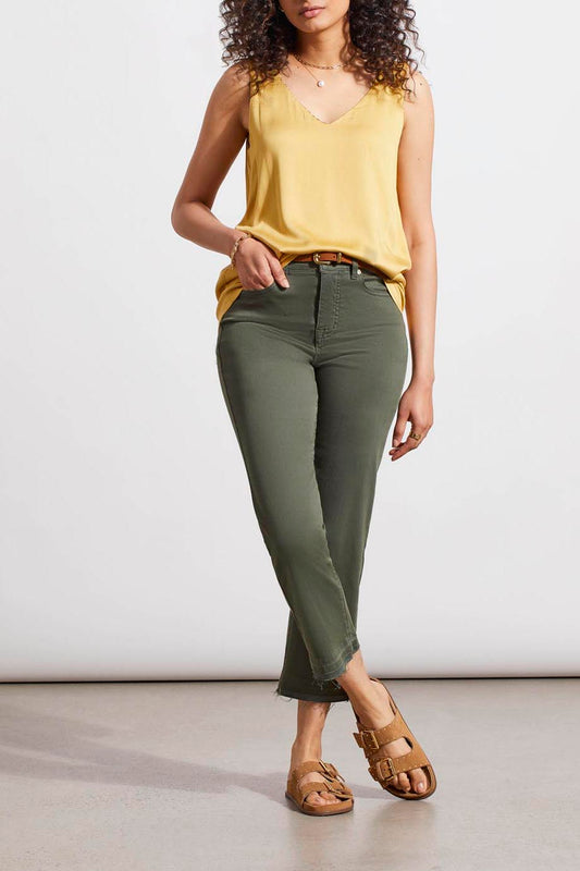 A woman in a Tribal Dijon Reversible V-Neck Cami and green jeans stands against a neutral background, accessorized with a gold necklace and brown sandals.