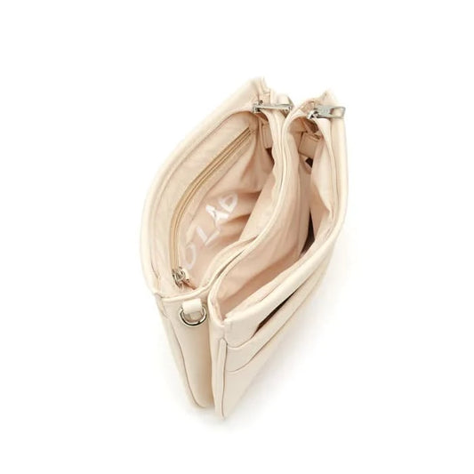 A person wearing a light gray blouse and beige pants carries Co-Lab’s The Nina Crossbody, an eco-friendly light green recycled vegan leather bag.