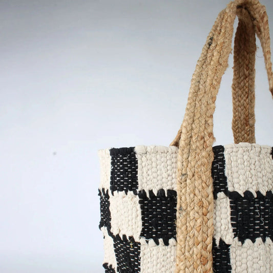 The Co-Lab Laguna Beach Tote Bag showcases a chic black-and-white checkerboard pattern and a sturdy woven jute handle, standing upright against a plain background.