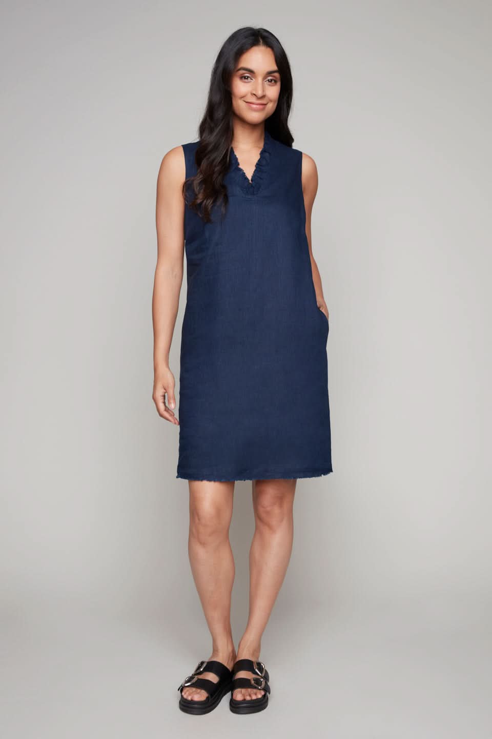 A person stands wearing Carre Noir's V Neck Ruffled Linen Dress and black sandals on a plain background.