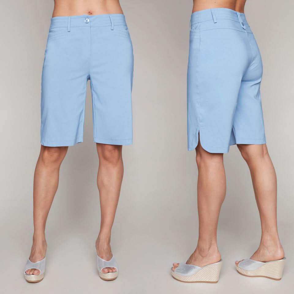 A woman models Carre Noir Bermuda Shorts in Denim Blue, showing both front and back views, paired with silver wedge sandals. These versatile shorts are a stylish and practical choice for any sunny day occasion.