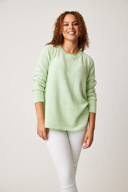 Woman smiling in a Cotton Country Skyler Sweatshirt and white pants against a neutral background.