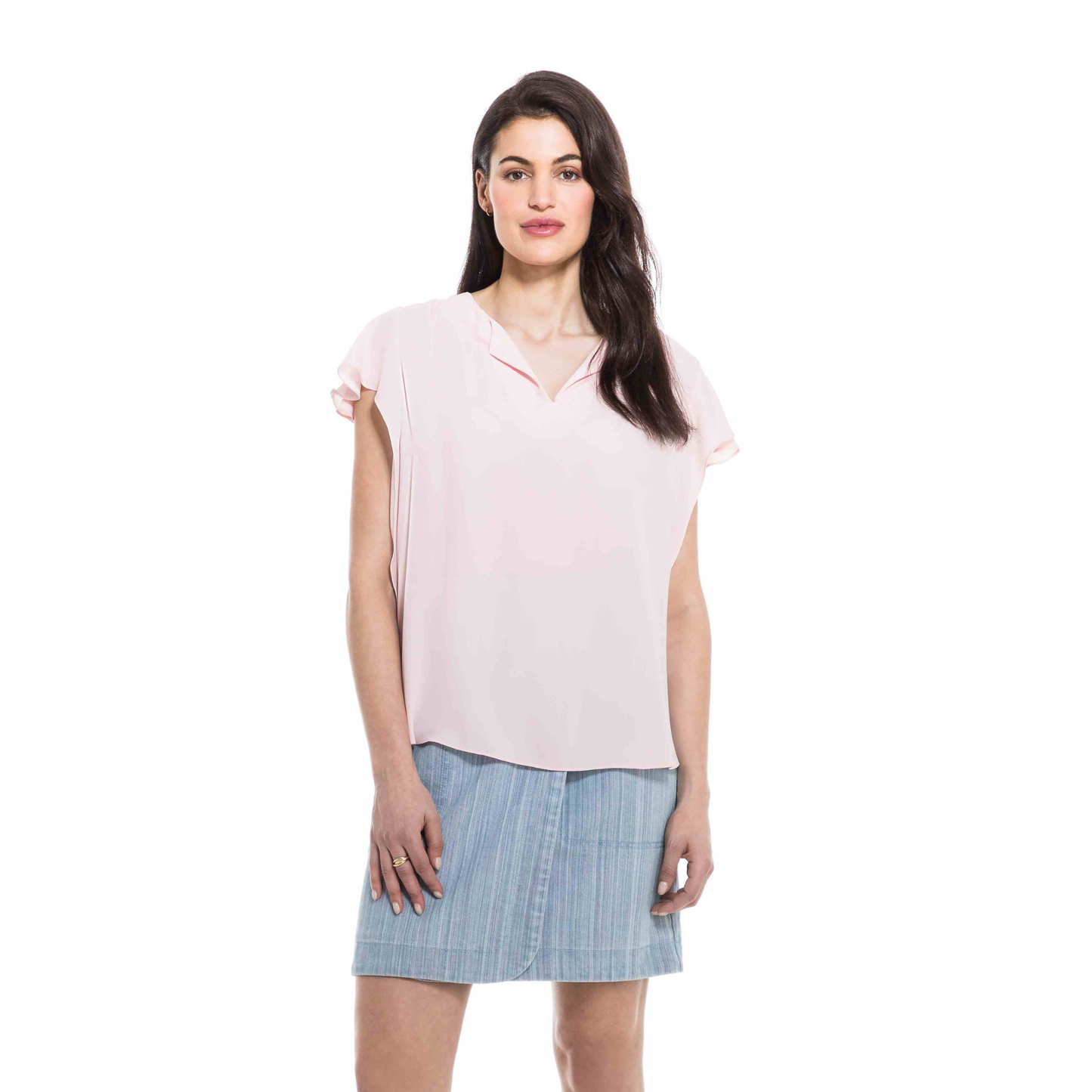 A woman standing against a white background, wearing an Orly Blush Collared Blouse and a blue striped skirt, perfectly encapsulating spring fashion.