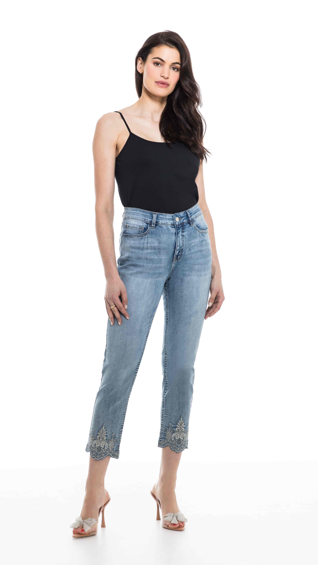 Woman wearing fashionable, Orly embellished cropped denim jeans with detailed hem and high heels standing against a white background.