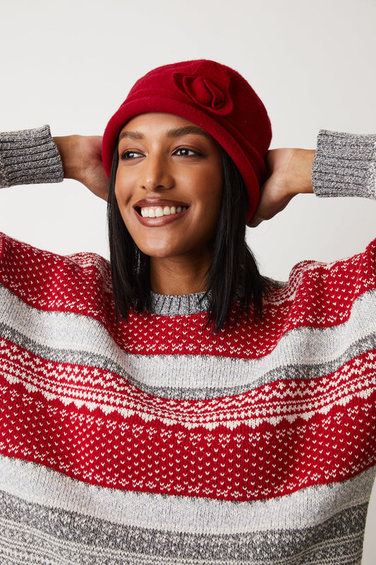 A young woman wearing a red Cotton Country Brighton Fairisle Crew | Grey Red sweater and hat, embracing the winter spirit with a cozy wool blend.