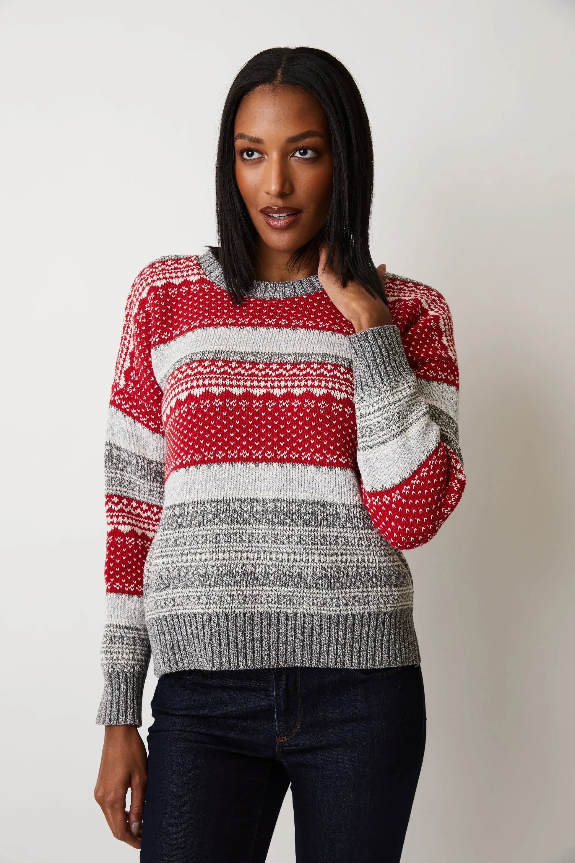 A young woman wearing a red Cotton Country Brighton Fairisle Crew | Grey Red sweater and hat, embracing the winter spirit with a cozy wool blend.