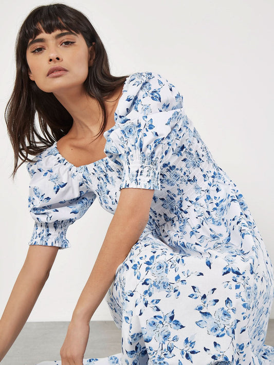 A person wearing the Apricot Smock Milk Maid Cotton Dress, seated with a neutral expression, looks at the camera.