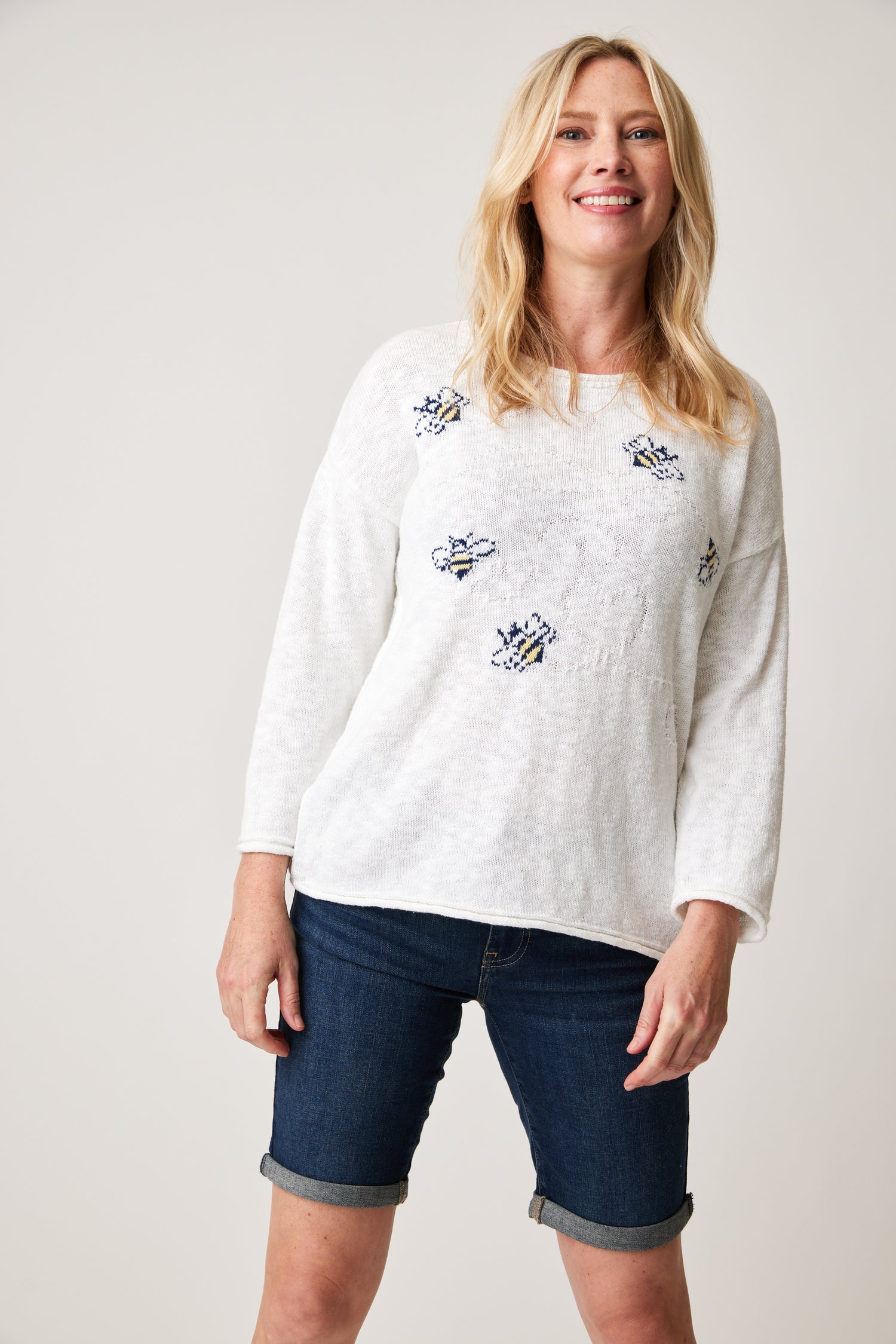 A woman wearing a Cotton Country Busy Bee Sweater and denim shorts.