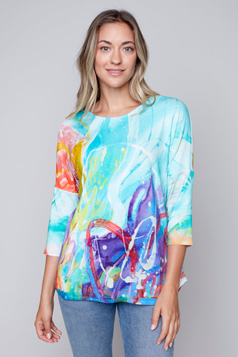A woman wearing a Colorful Abstract Knitted Top by Claire Desjardins, paired with jeans.