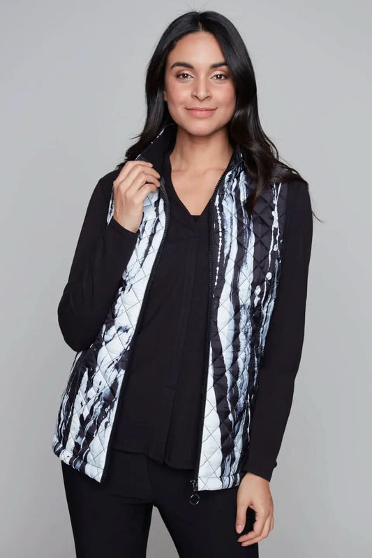 A person with long hair is wearing a black shirt and a stylish Claire Desjardins Quilted Black & White Vest. They are holding the vest's zipper. The background is plain and neutral.