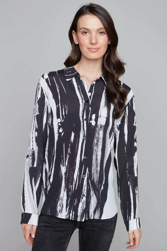 A person wearing a stylish Abstract Woven Blouse by Claire Desjardins, featuring a black and white pattern with long sleeves, paired with black pants, stands against a gray background.