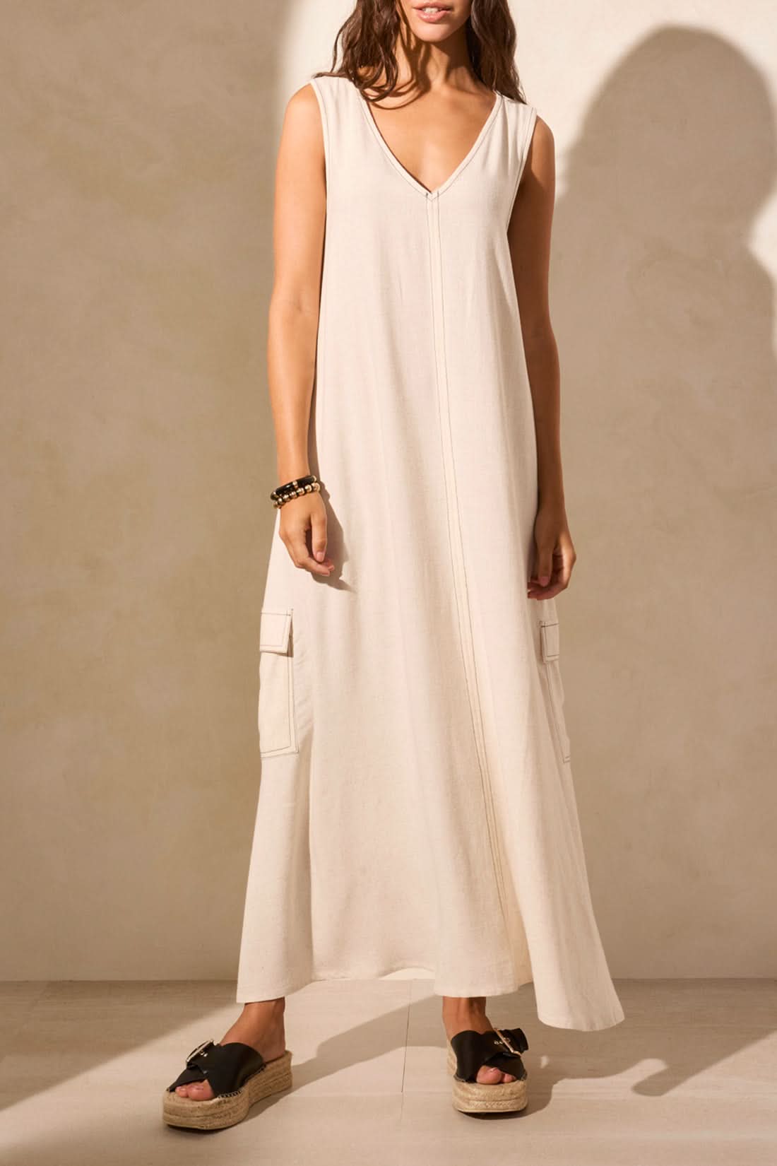 A woman stands against a plain backdrop in Tribal's Sleeveless V-Neck Cargo Dress, exuding effortless fashion. Her right hand rests at her side as the minimalist elegance is captured with her left arm out of frame.