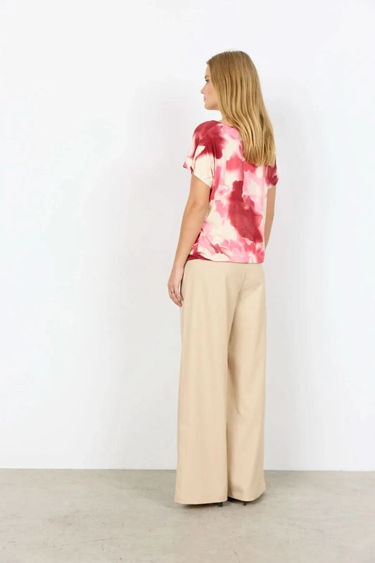 A woman faces away, wearing the pink and white tie-dye Marica Top by Soya Concepts with beige wide-leg pants, set against a plain white background.