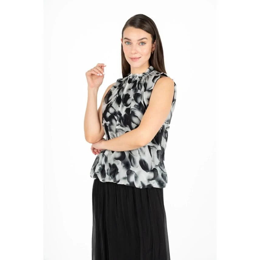 A woman is shown from the back wearing the Black Flowing Petals Blouse by M Made In Italy, featuring a sleeveless design and a high neckline with a black and white floral pattern.