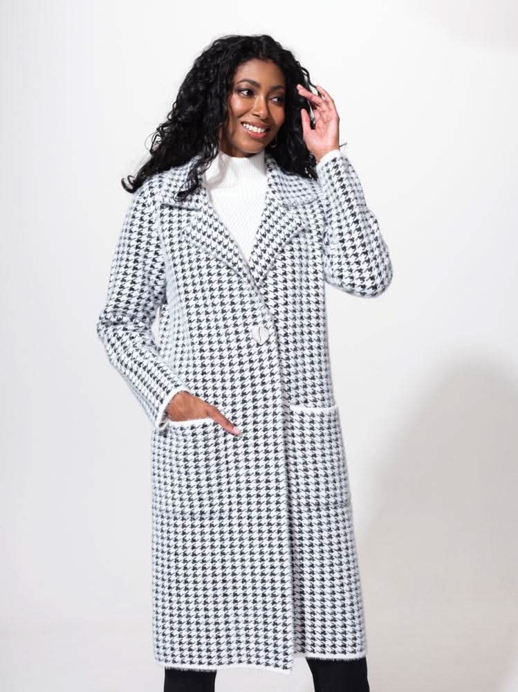 A woman in an Alison Sheri Houndstooth Jacket smiles while posing, her hand adjusting her hair. She pairs it with a white turtleneck sweater underneath, adding the perfect touch to her cold-weather accessory ensemble.
