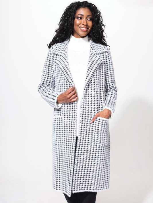 A woman in an Alison Sheri Houndstooth Jacket smiles while posing, her hand adjusting her hair. She pairs it with a white turtleneck sweater underneath, adding the perfect touch to her cold-weather accessory ensemble.