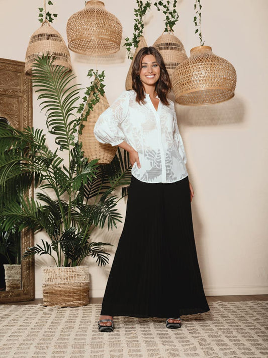 A fashion-forward woman wearing a white blouse and Alison Sheri's Pleated Super Wide Leg Pants with a folded design.