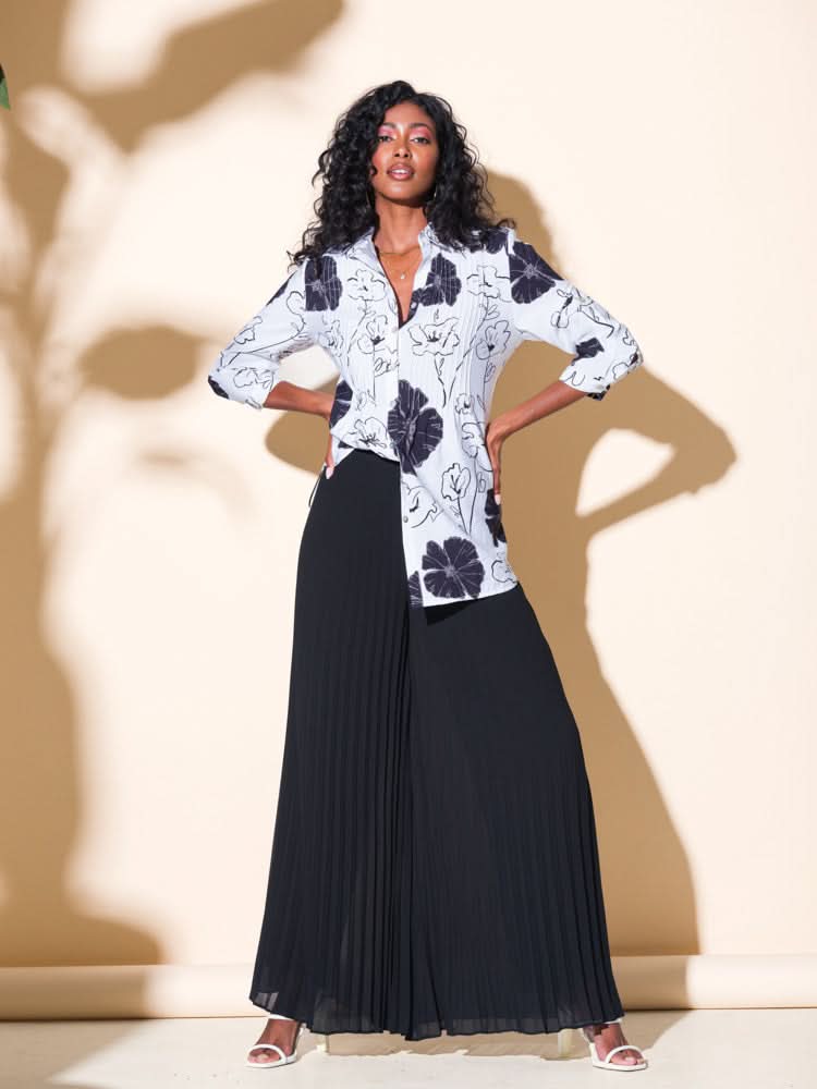 A fashion-forward woman wearing a white blouse and Alison Sheri's Pleated Super Wide Leg Pants with a folded design.