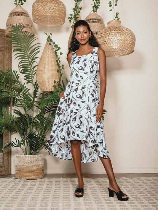 A woman in an Alison Sheri black and white Tulip Print Square Neck High Low Dress with Pockets standing in front of a potted plant.