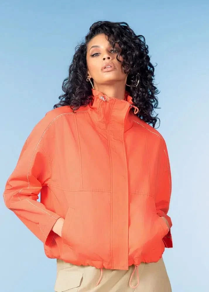Model wearing the Alison Sheri Coral Spring Jacket with hands in pockets, standing against a light blue background.
