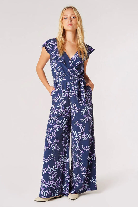 Woman standing in a blue floral Apricot Wrap Palazzo Jumpsuit with a v-neckline and wide-leg design, perfect for a versatile summer wardrobe.