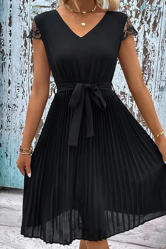 Black pleated midi dress with lace-up cap sleeves and a ribbon belt on a model against a rustic blue wooden background. 

Product: Black Lace Sleeves Waist Lace Up Smocked Dress
Brand: Don't Be Chy Boutique