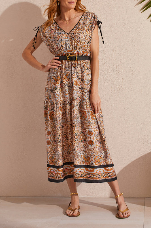 Woman posing in a Tribal Border Print Maxi Dress With Shoulder Ties and waist belt, accessorized with gold sandals.