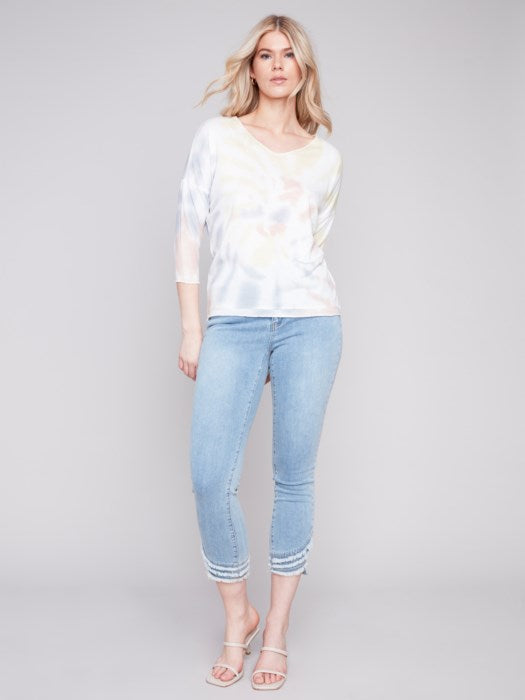 A woman in a stylish, Charlie B Indigo Printed V Neck Top and blue jeans standing against a neutral background.
