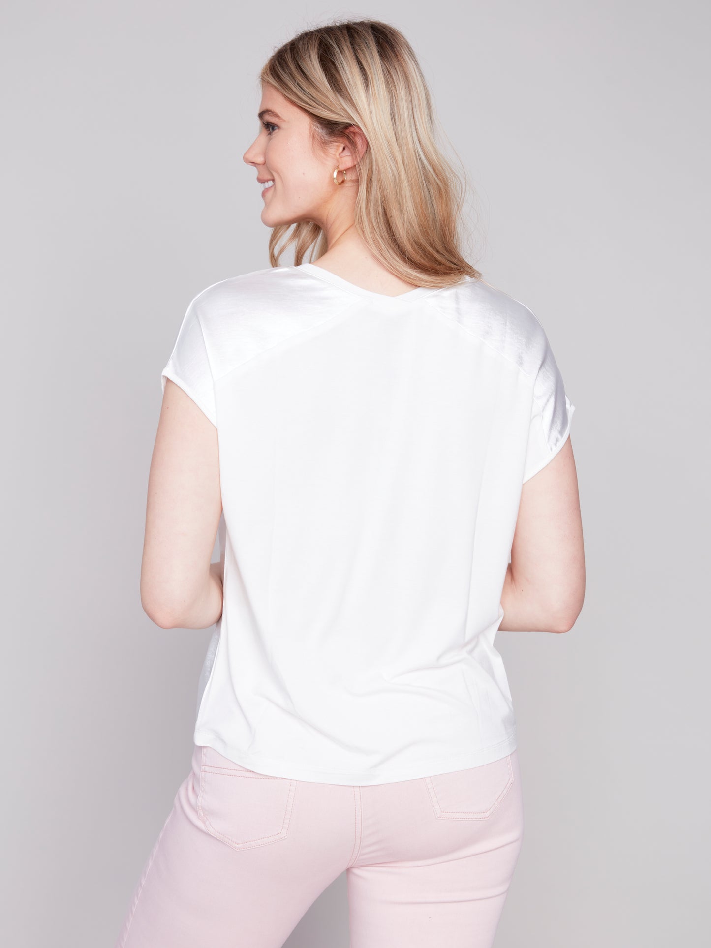 Woman in a Charlie B satin knit combo V-neck top and pink pants posing against a grey background.